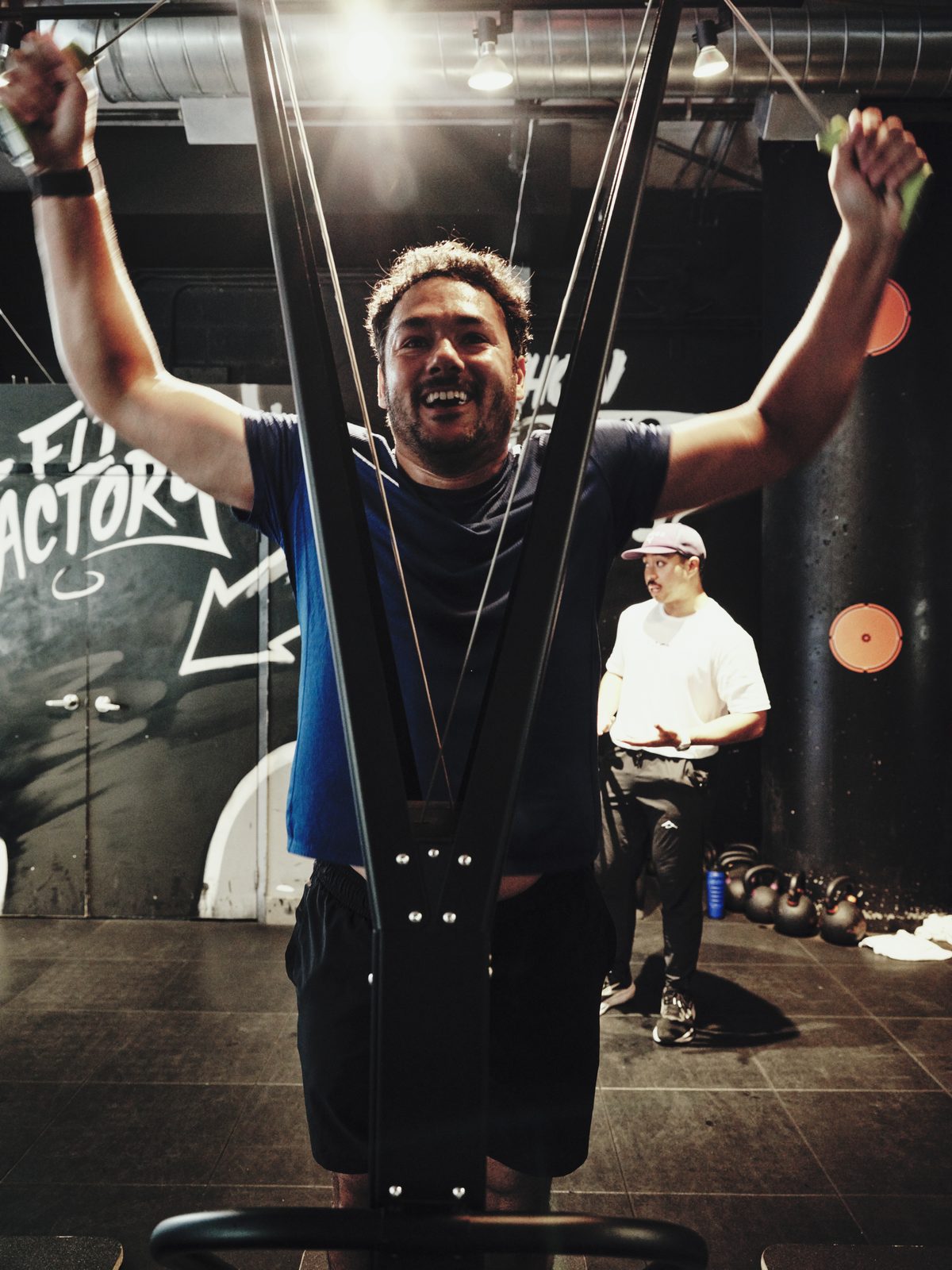 A smiling participant raises both handles on a SkiErg during a HYROX simulation at Fit Factory Downtown