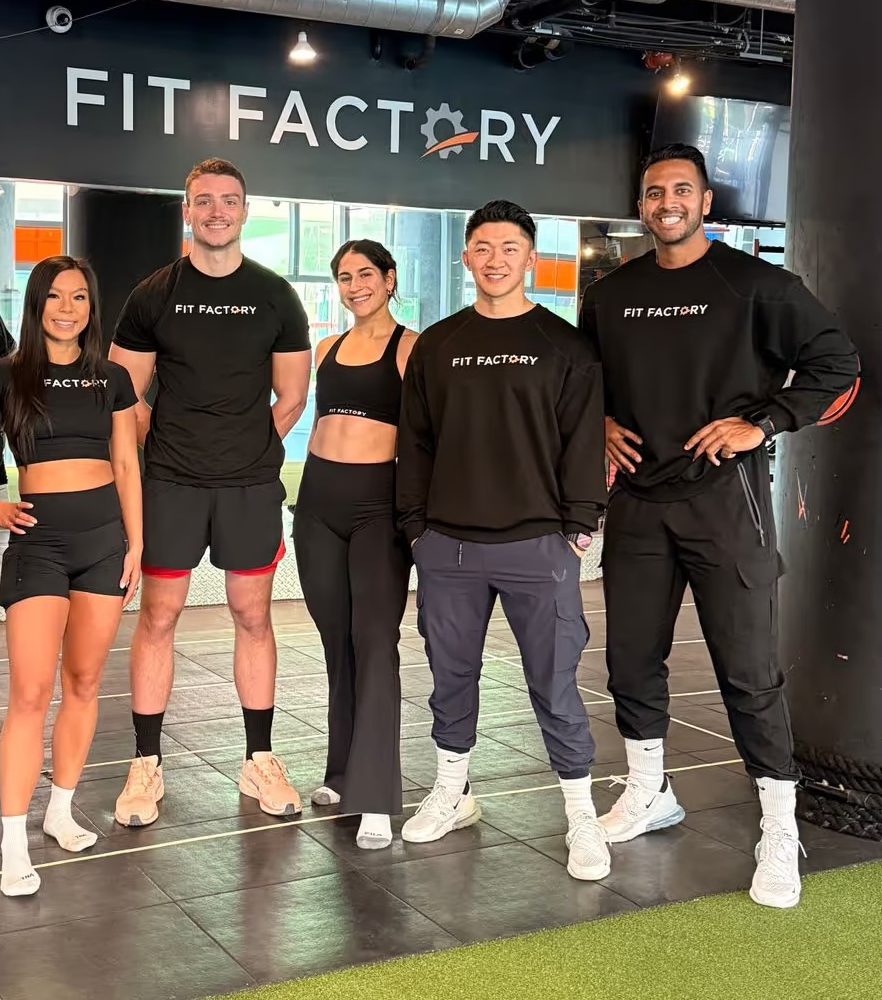 Fit Factory Downtown coaches smiling together under the Fit Factory sign in the studio