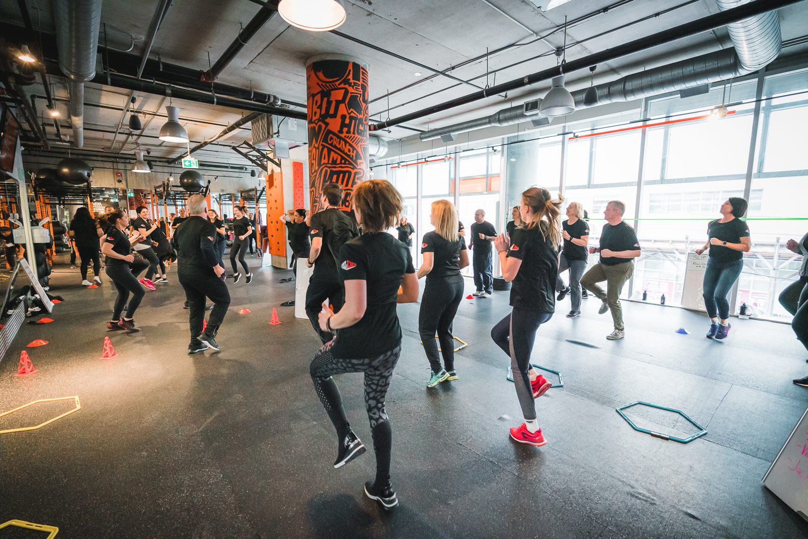About 25 people in matching event T-shirts warm up together across the Fit Factory Downtown training floor