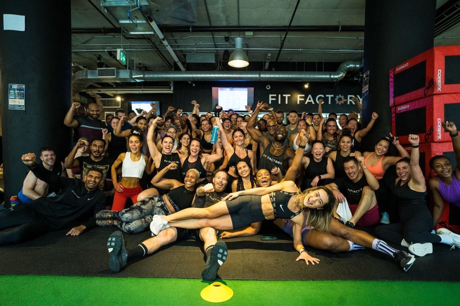 More than 60 members and coaches cheer under the Fit Factory sign after a packed class at the Downtown studio