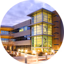 Modern three-story building with large glass windows and illuminated exterior lights at dusk.