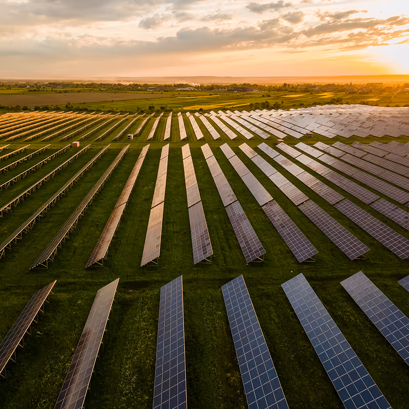 A vast solar farm with multiple rows of solar panels under a partly cloudy sky at sunset.