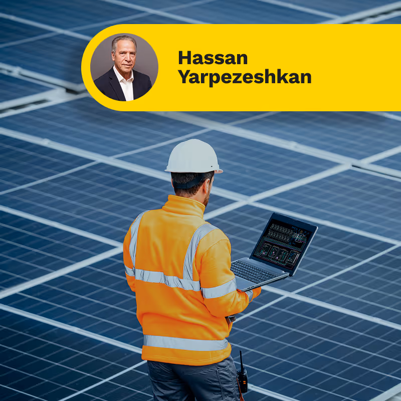 Engineer in orange safety jacket and white helmet inspecting solar panels with a laptop.