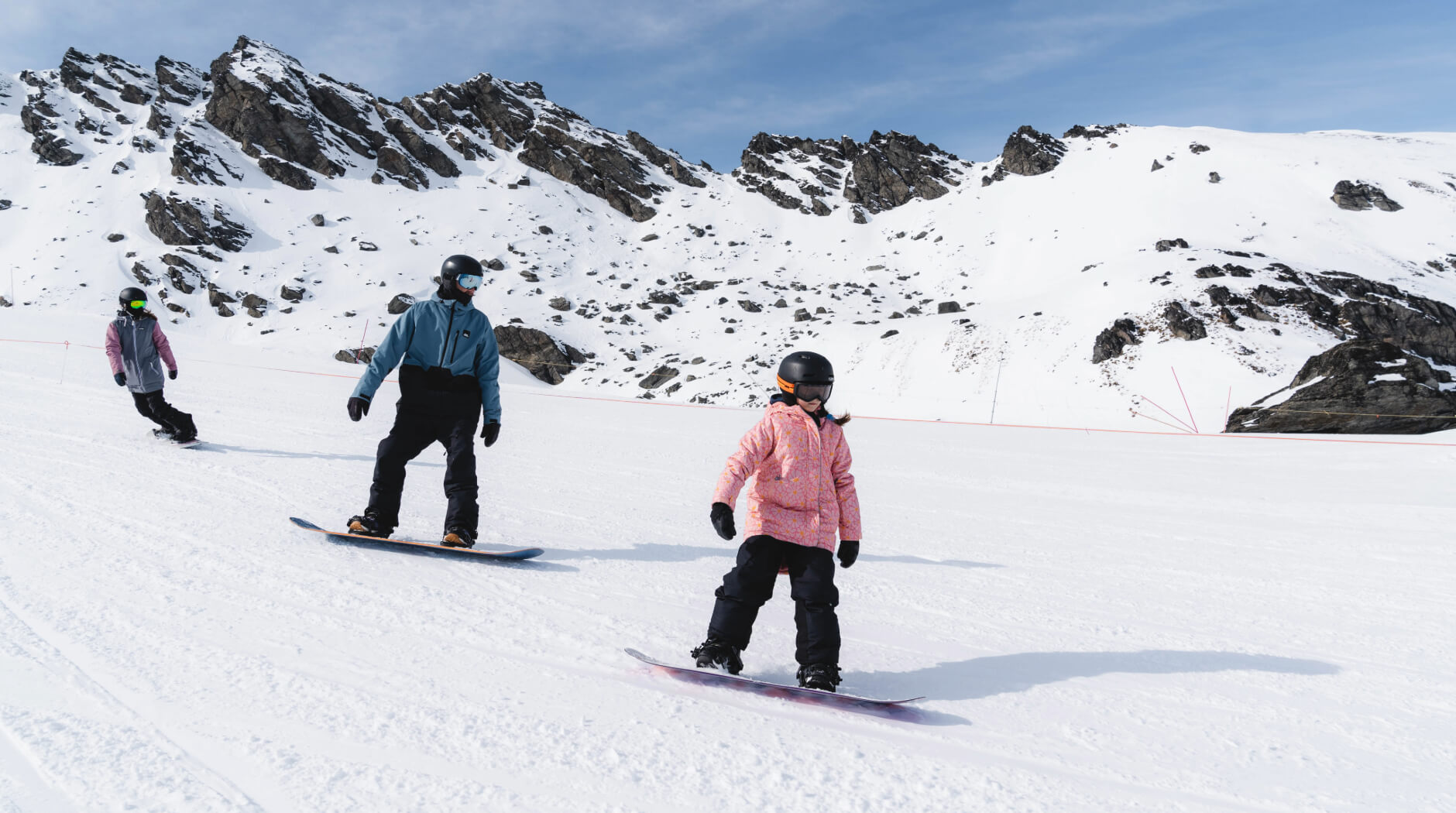 Family learning to snowboard together on a gentle slope at Mt Hutt