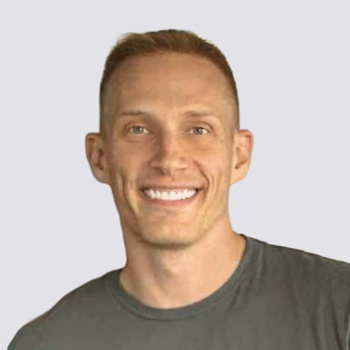 Smiling man with short light brown hair wearing a gray shirt against a plain background.