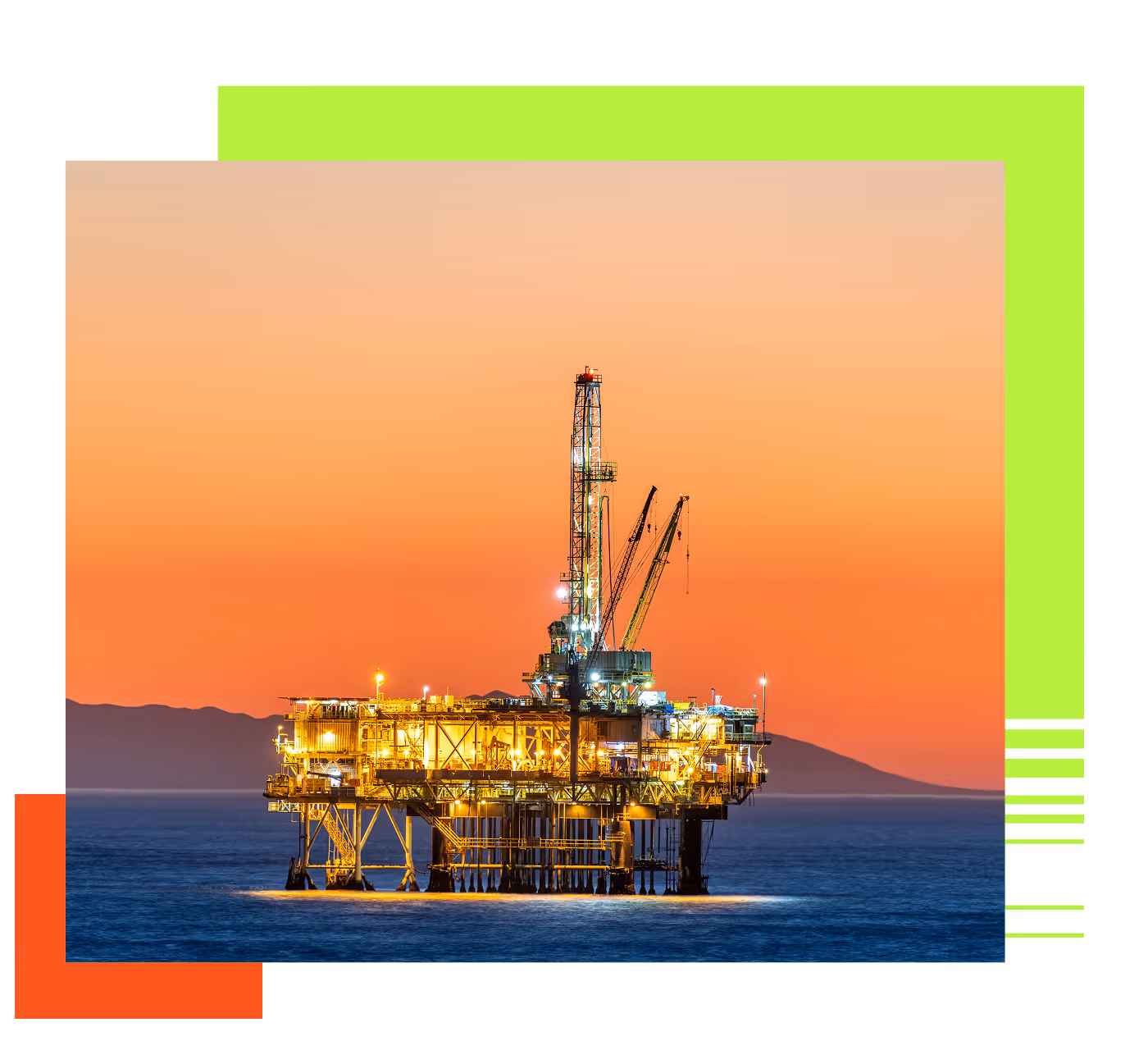 Illuminated offshore oil drilling platform in the ocean at sunset with mountains in the background.