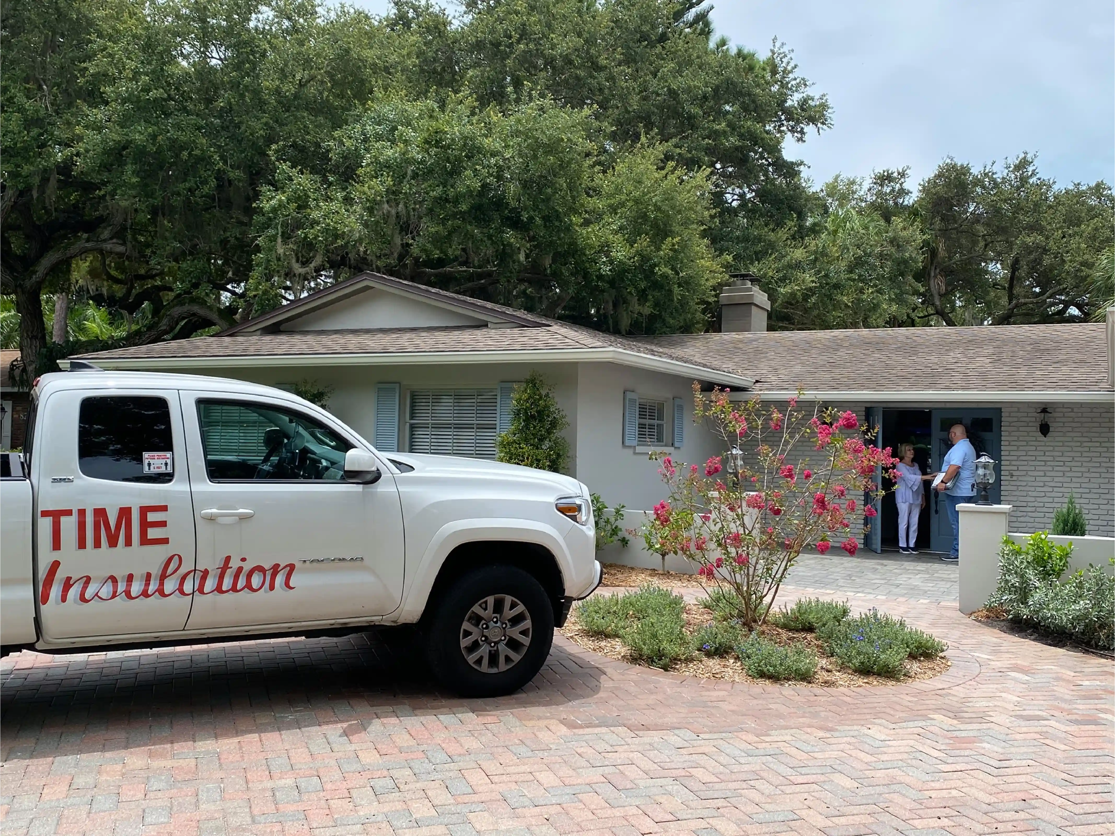 White pickup truck with 'TIME Insulation' parked outside a house where two people stand and talk at the front door.