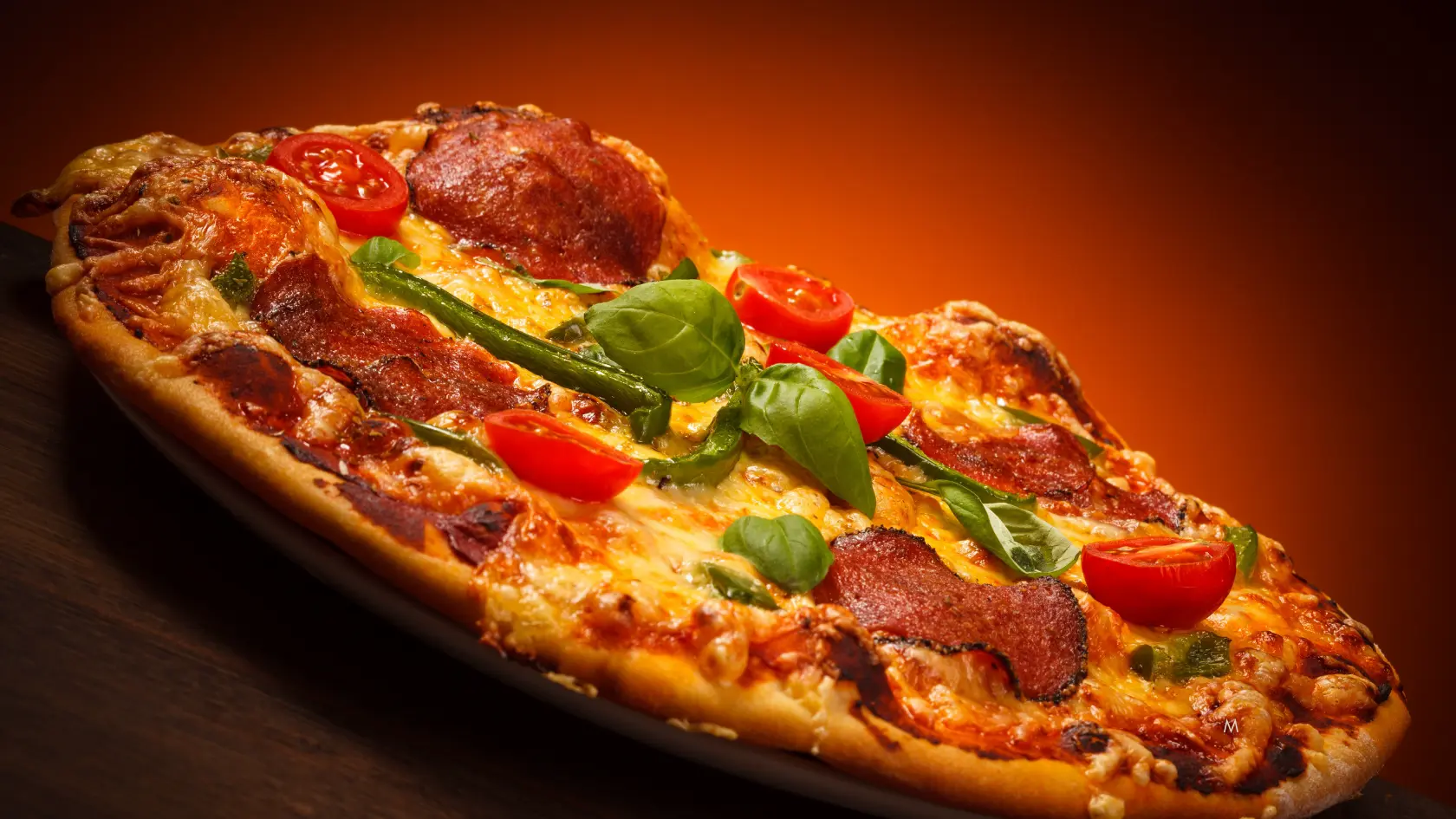A freshly baked pepperoni pizza with cherry tomatoes and basil leaves, served on a wooden table.