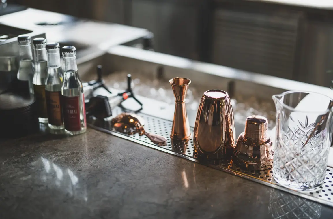 A neatly arranged bartending workstation with copper cocktail shakers, jiggers, glassware, and bottles, ready for mixing drinks.