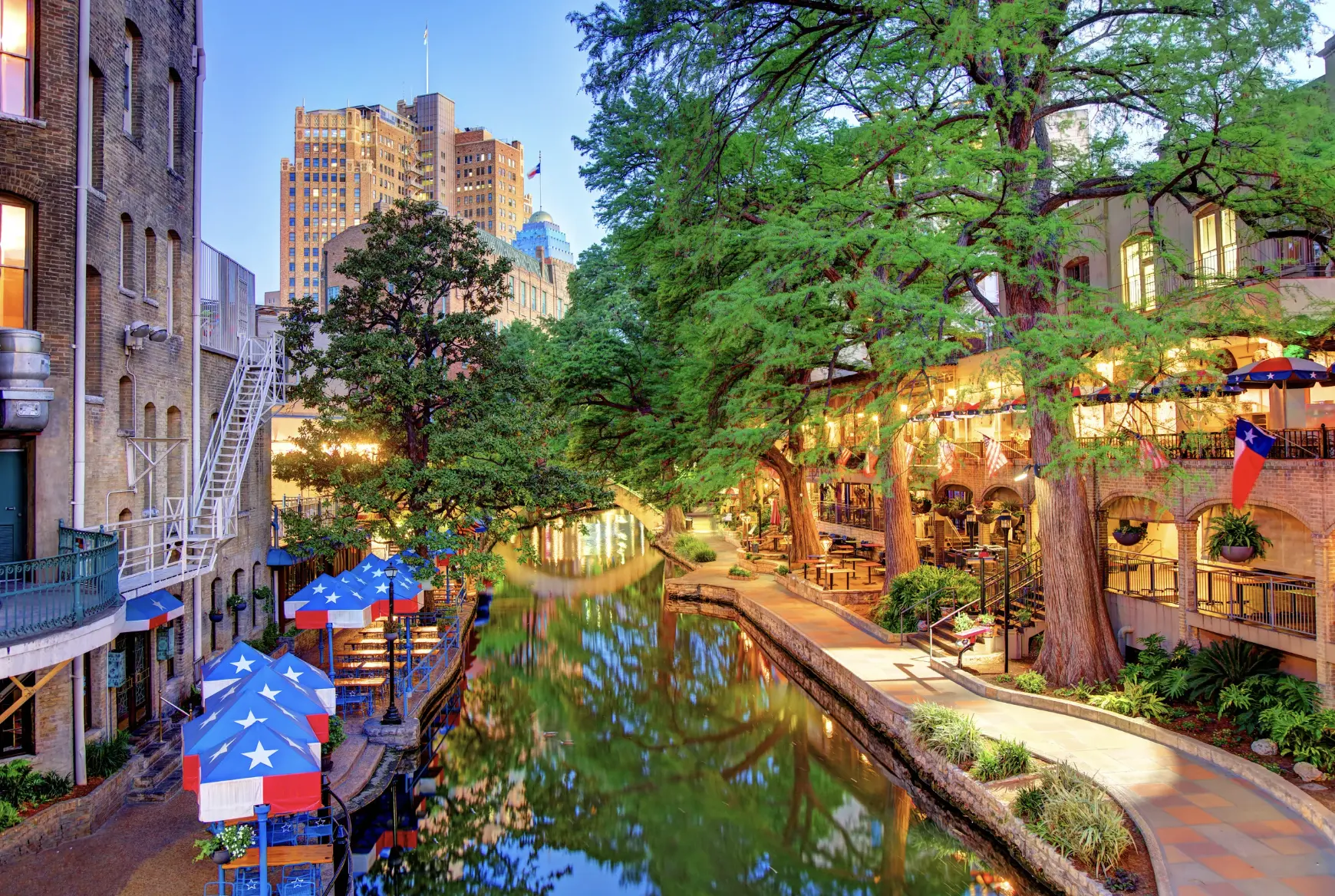 "Vibrant River Walk scene in San Antonio with outdoor dining and colorful umbrellas by the water"