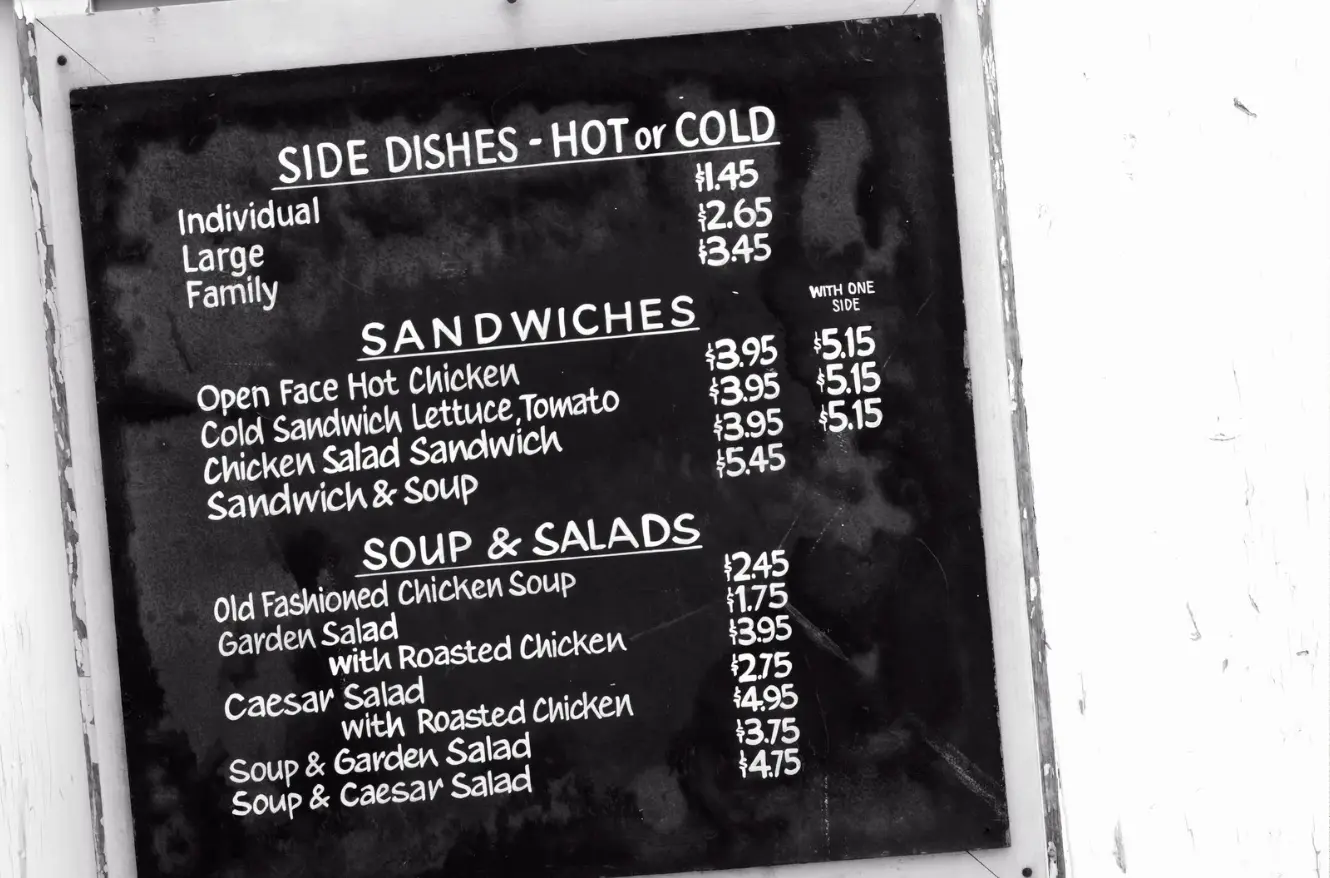 A vintage black-and-white chalkboard menu displaying sandwich, soup, and salad options with handwritten-style text.