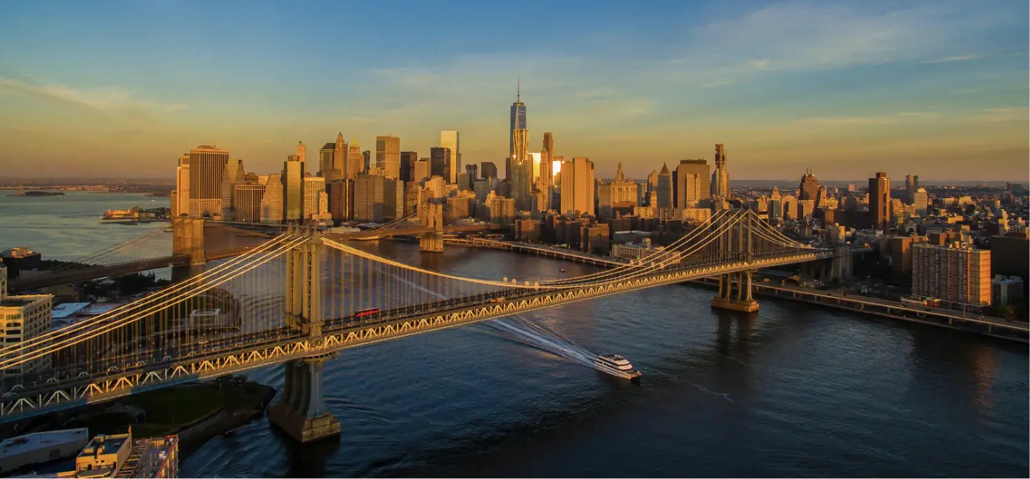 Aerial view of the Manhattan skyline at sunset, featuring the Brooklyn and Manhattan Bridges over the East River in New York City.
