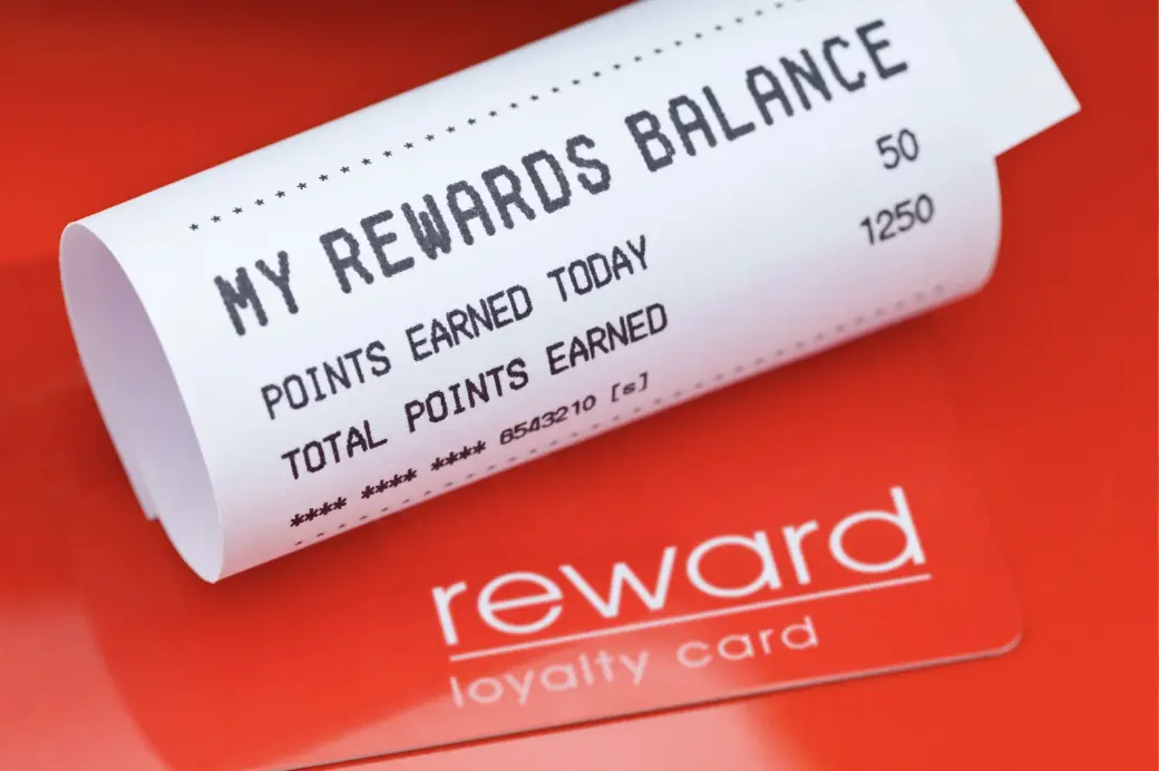 A receipt showing a customer’s earned reward points placed on a red background with a loyalty card.