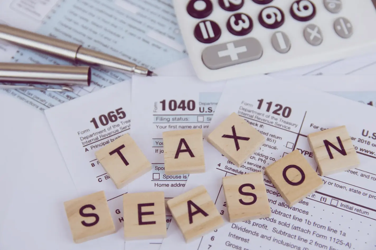 "Wooden letter tiles spelling 'Tax Season' placed on top of various IRS tax forms and financial documents."
