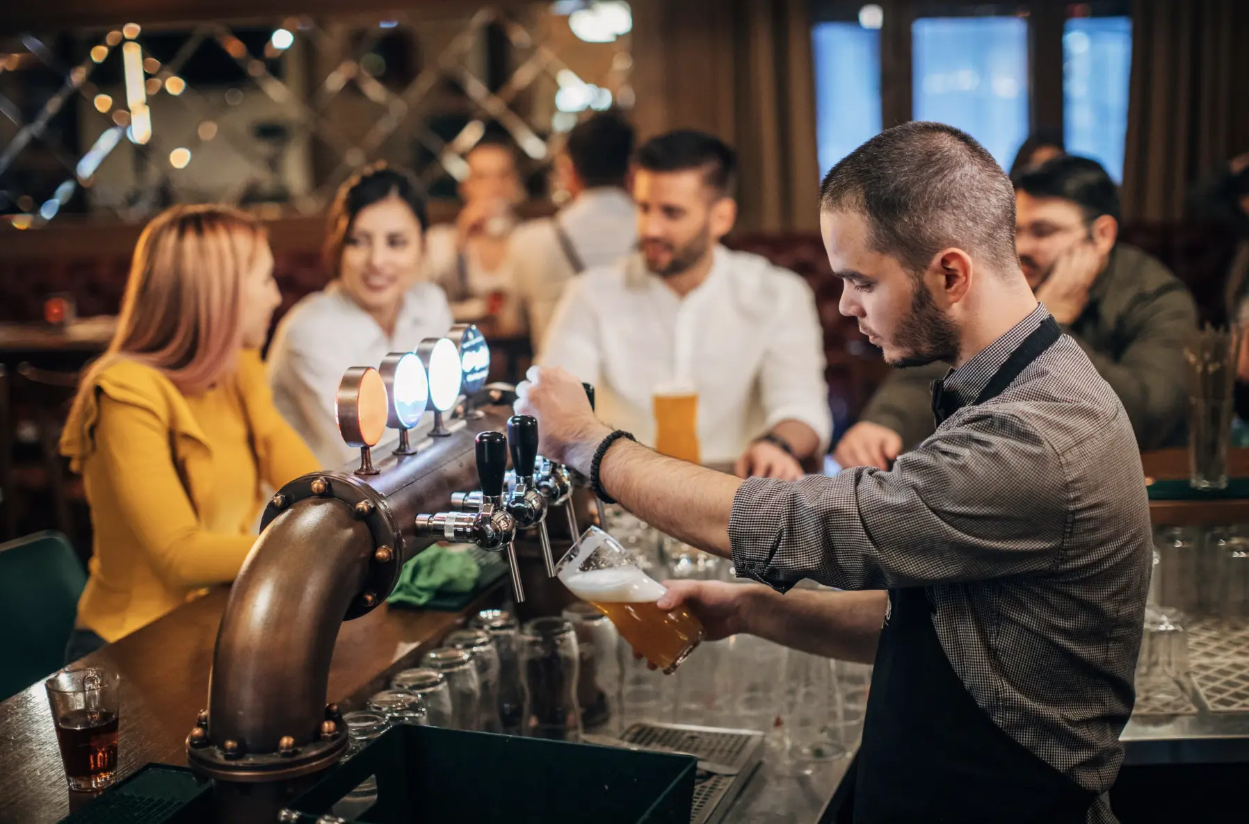 A bartender pouring a draft beer at a lively bar, demonstrating key barback responsibilities in keg management and customer service support.