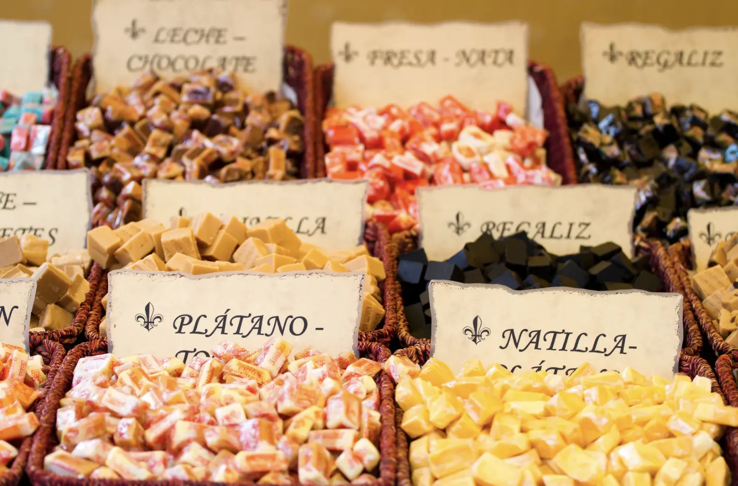 An assortment of colorful candies and caramels in labeled baskets at a market or confectionery shop.