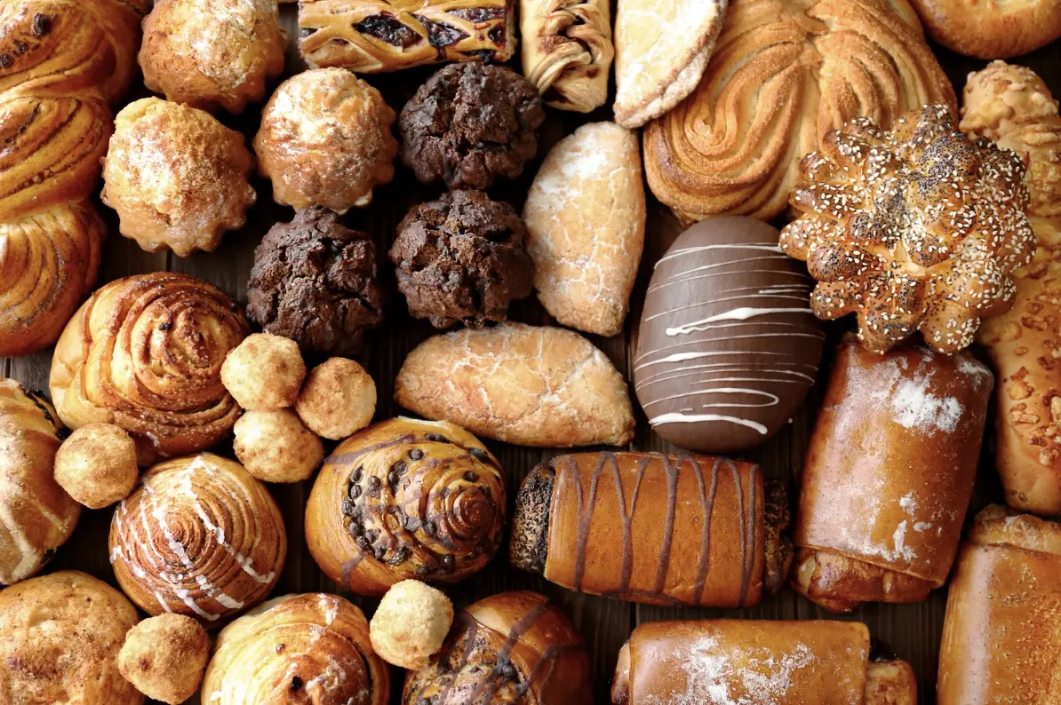 A collection of freshly baked pastries, including croissants, muffins, and bread rolls, displayed on a wooden surface.