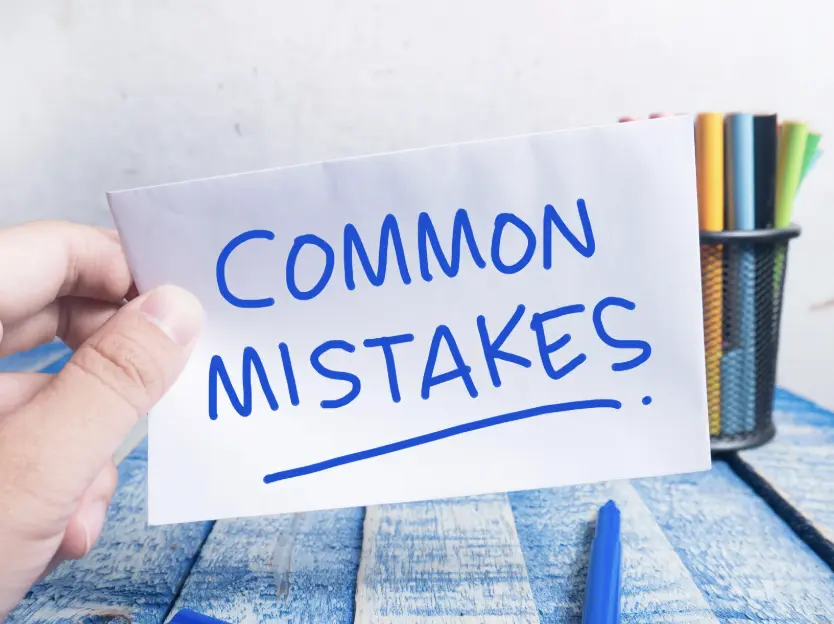 A hand holding a paper note written "COMMON MISTAKES" on a blue wooden table, emphasizing typical errors.