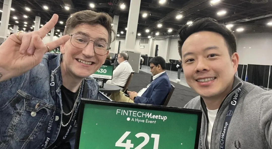 Two attendees posing for a photo at Fintech Meetup 2026 with a meeting table sign in the foreground.