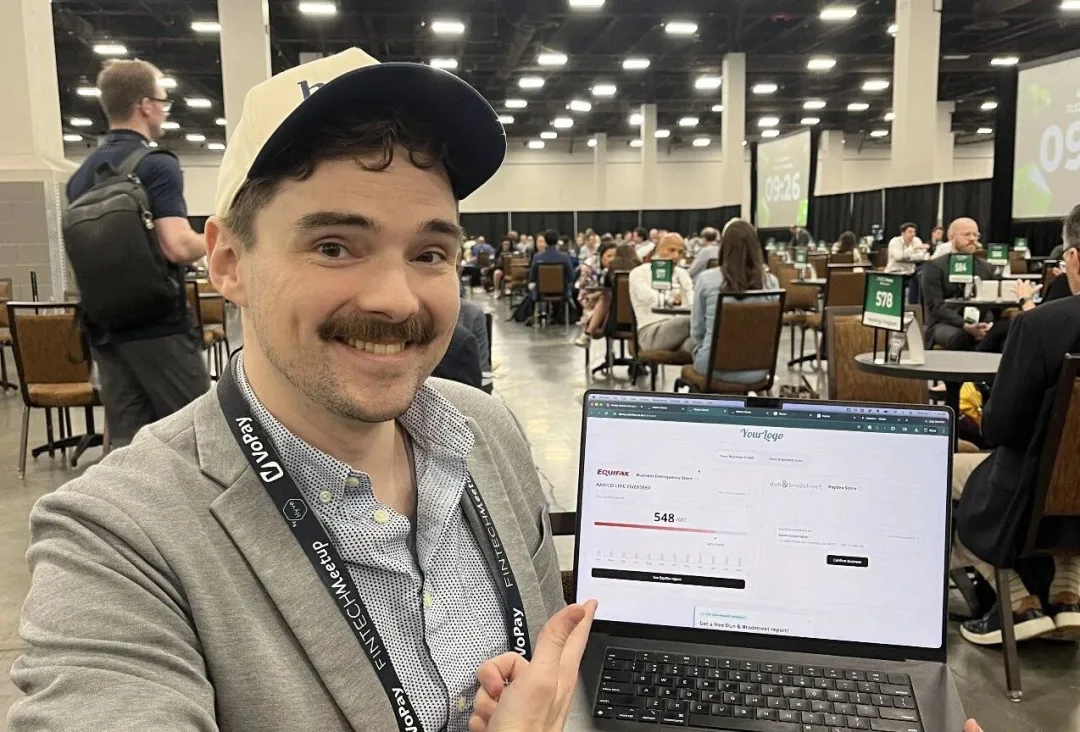 An attendee at Fintech Meetup 2026 smiling and showing a laptop screen with a lending or credit-related platform demo.