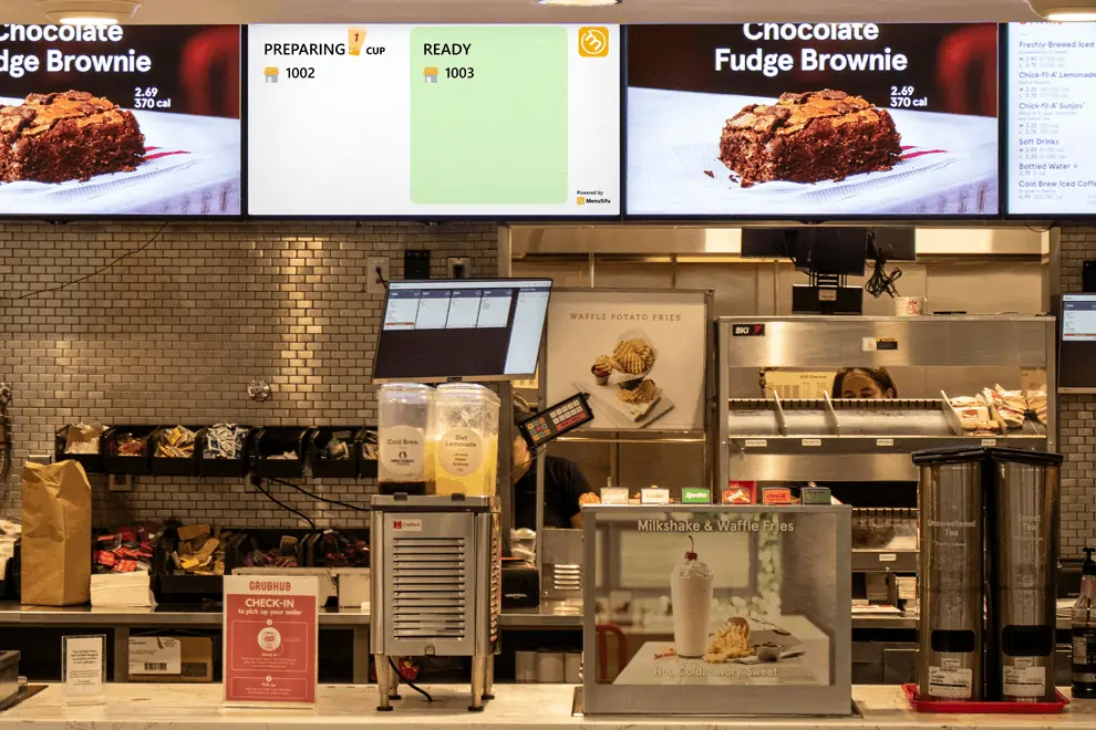Fast food restaurant counter with monitors displaying digital order queue.