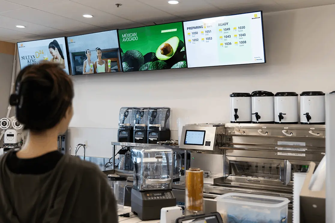 Customer looks at vibrant smart display with ads and order status updates.