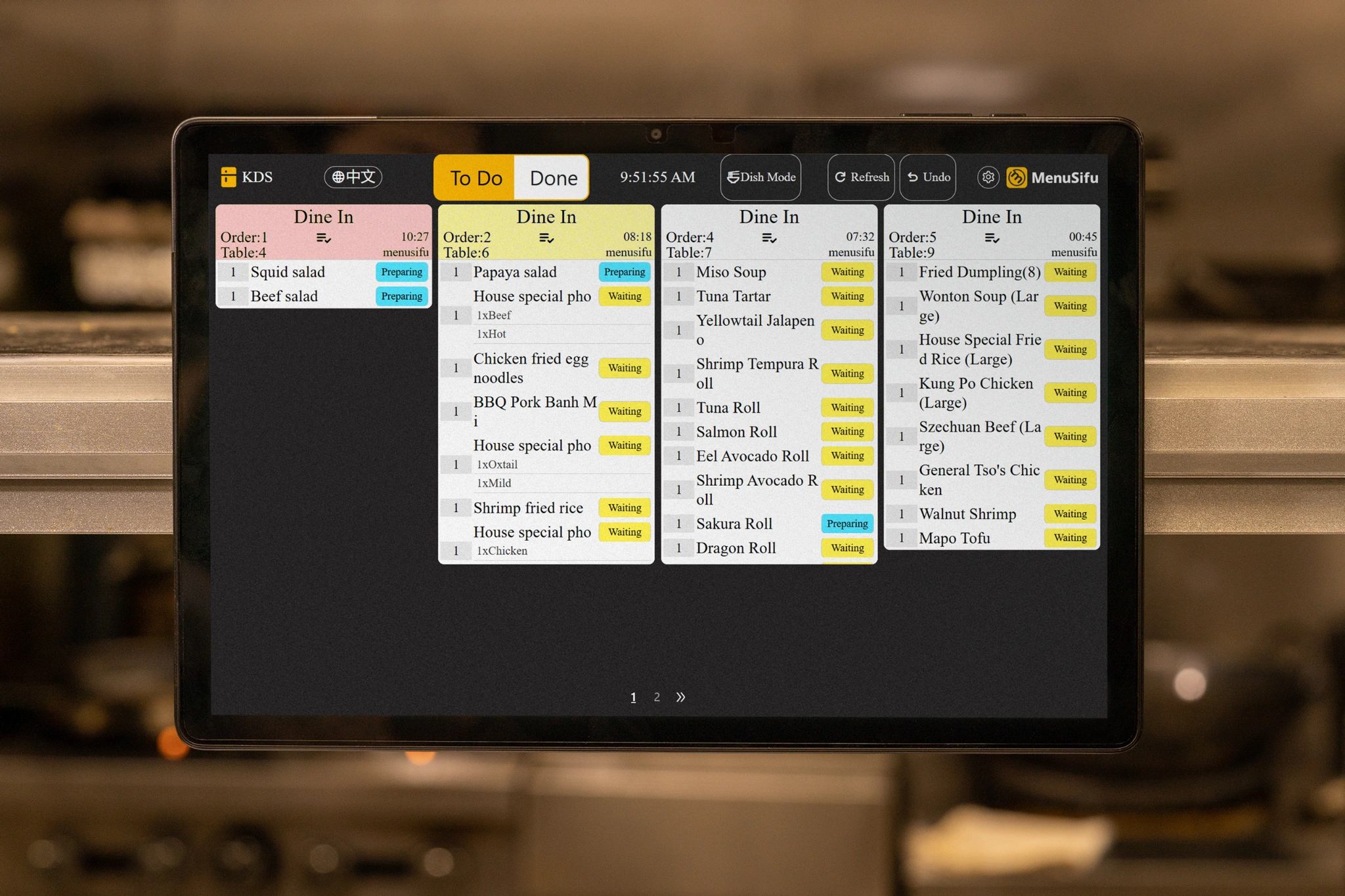 Kitchen display screen showing dine-in and to-go food orders with item names and recall buttons in a fast food restaurant.