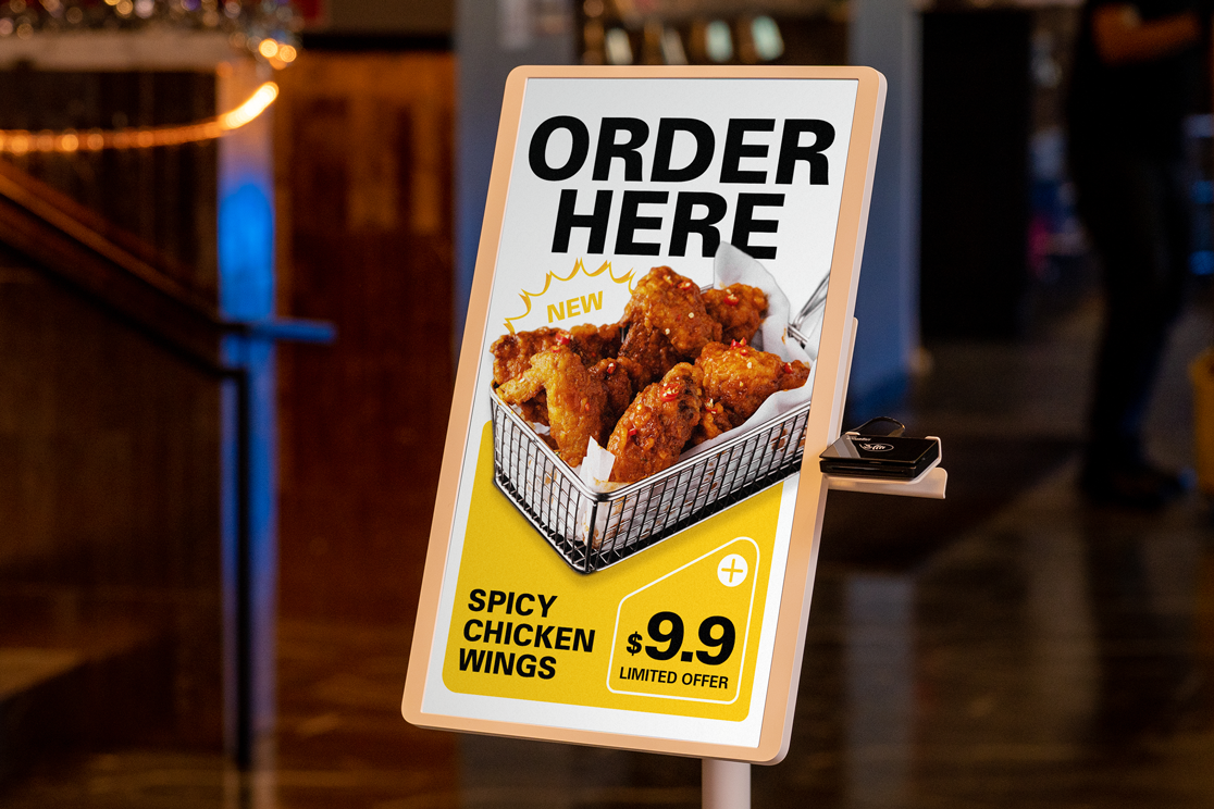 Digital kiosk displaying spicy chicken wings promo with “Order Here” and $9.9 offer in a fast food restaurant.