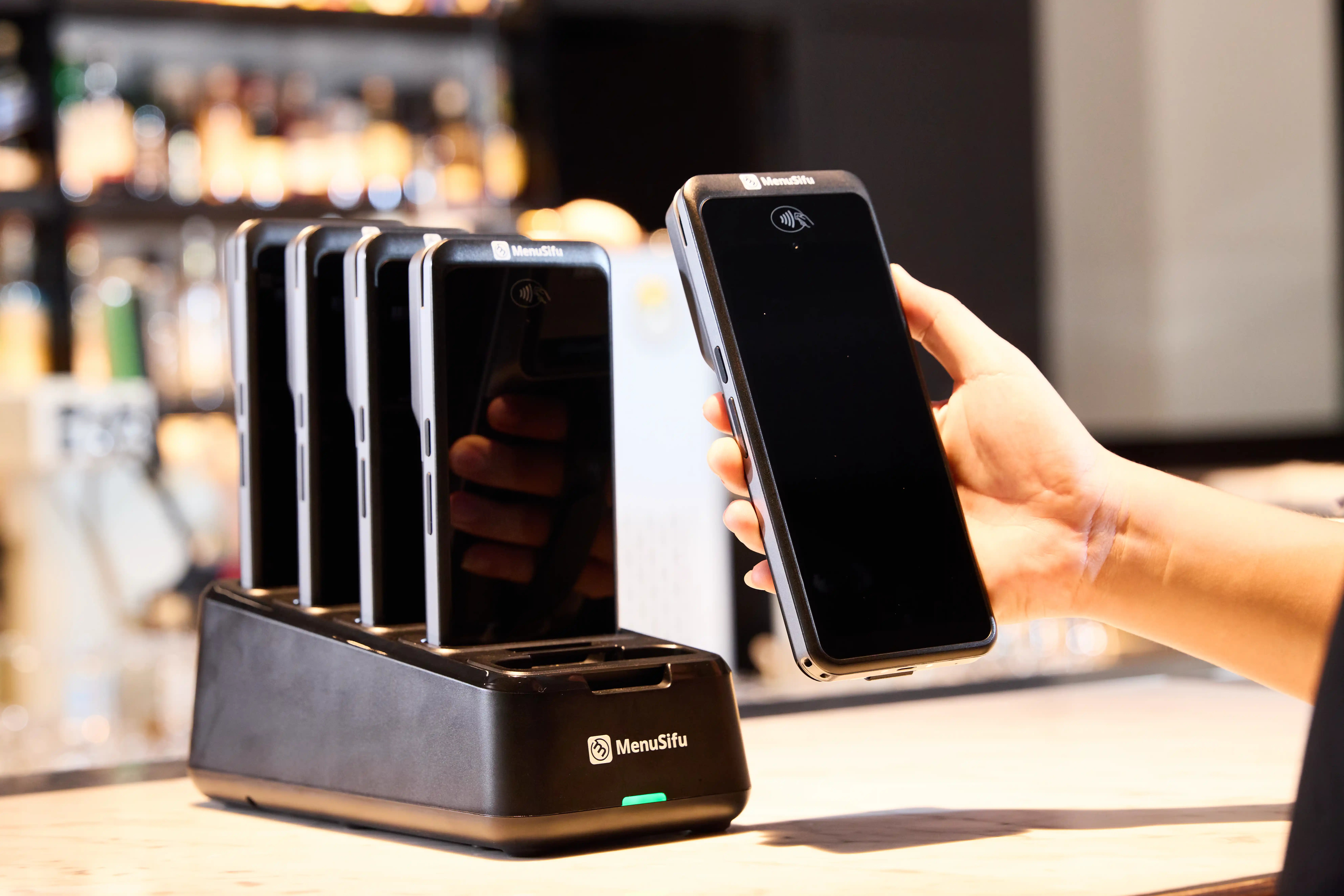 Restaurant employee removing a MenuSifu POS GO 2 handheld POS device from its charging dock