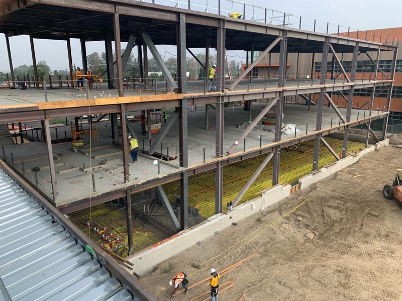 Multi-story steel frame under construction, with workers installing structural steel and floor decking at an active job site