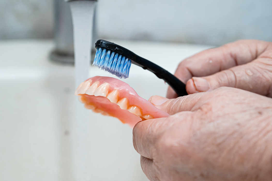 Close up of hands cleaning a denture with a toothbrush under running water