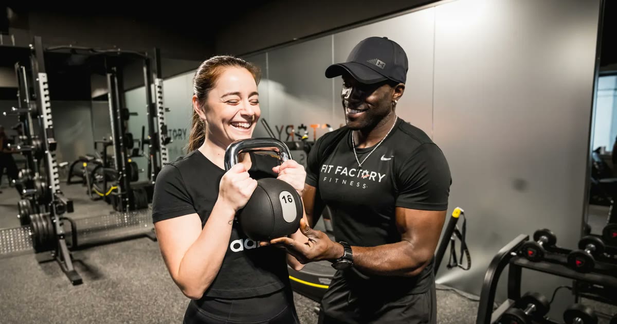 A Fit Factory coach and member smiling while the member holds a kettlebell in the goblet position