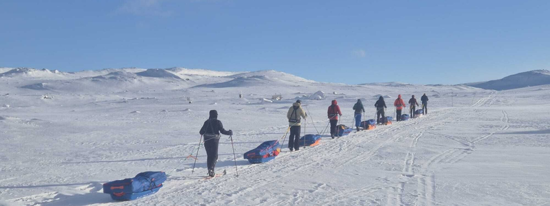 Group of people trekking across a snowy landscape pulling sleds, symbolizing teamwork, endurance, and a shared journey toward a common goal.