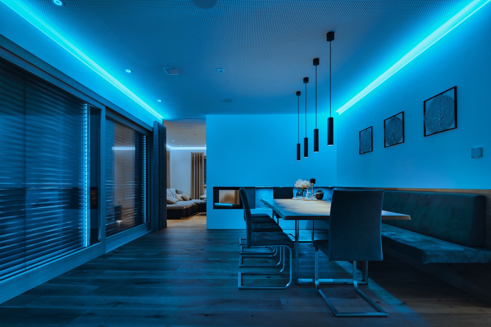 Nowoczesna jadalnia z szarymi krzesłami, drewnianym stołem i niebieskim oświetleniem LED przy suficie.