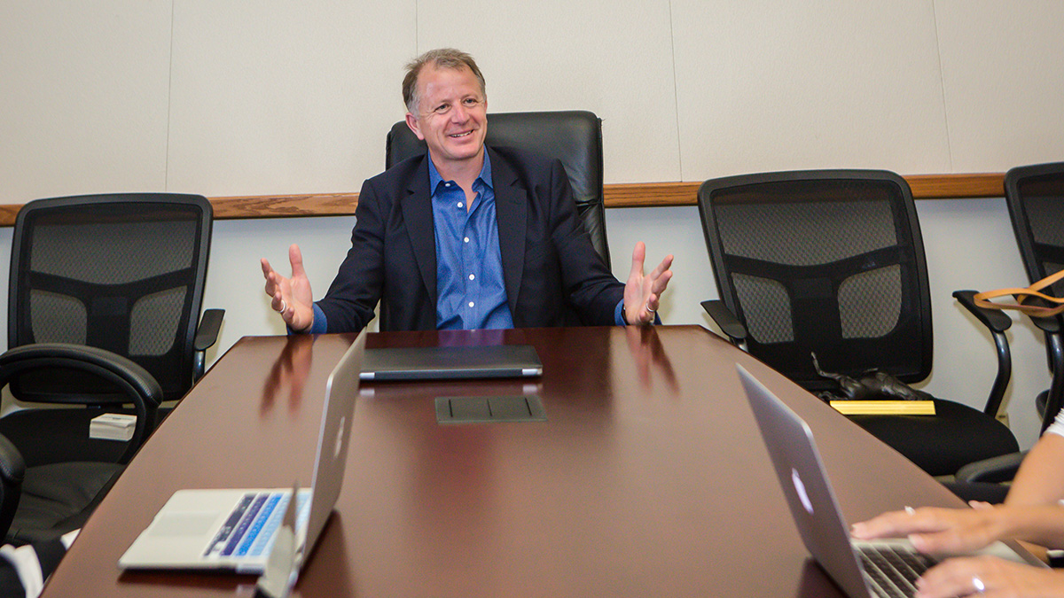 CEO Anthony Davies sitting at head of conference table, gesturing expansively and smiling