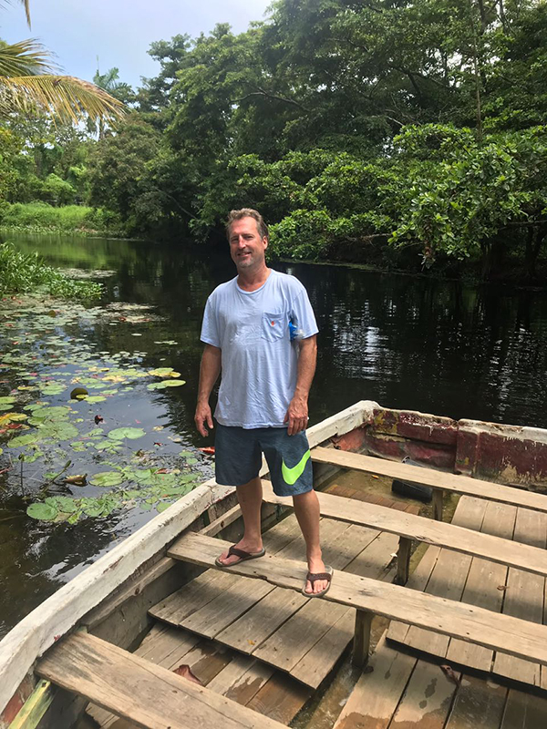 Scott standing in a small wooden boat surrounded by tropical vegetation and lily pads