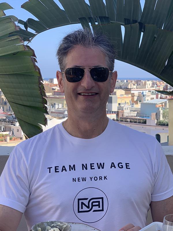 Todd standing outdoors in front of large tropical leaves with a coastal cityscape in the background.