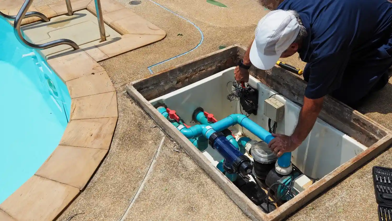 A technician installing pool and hot tub wiring and plumbing components within a concrete utility vault by a swimming pool.