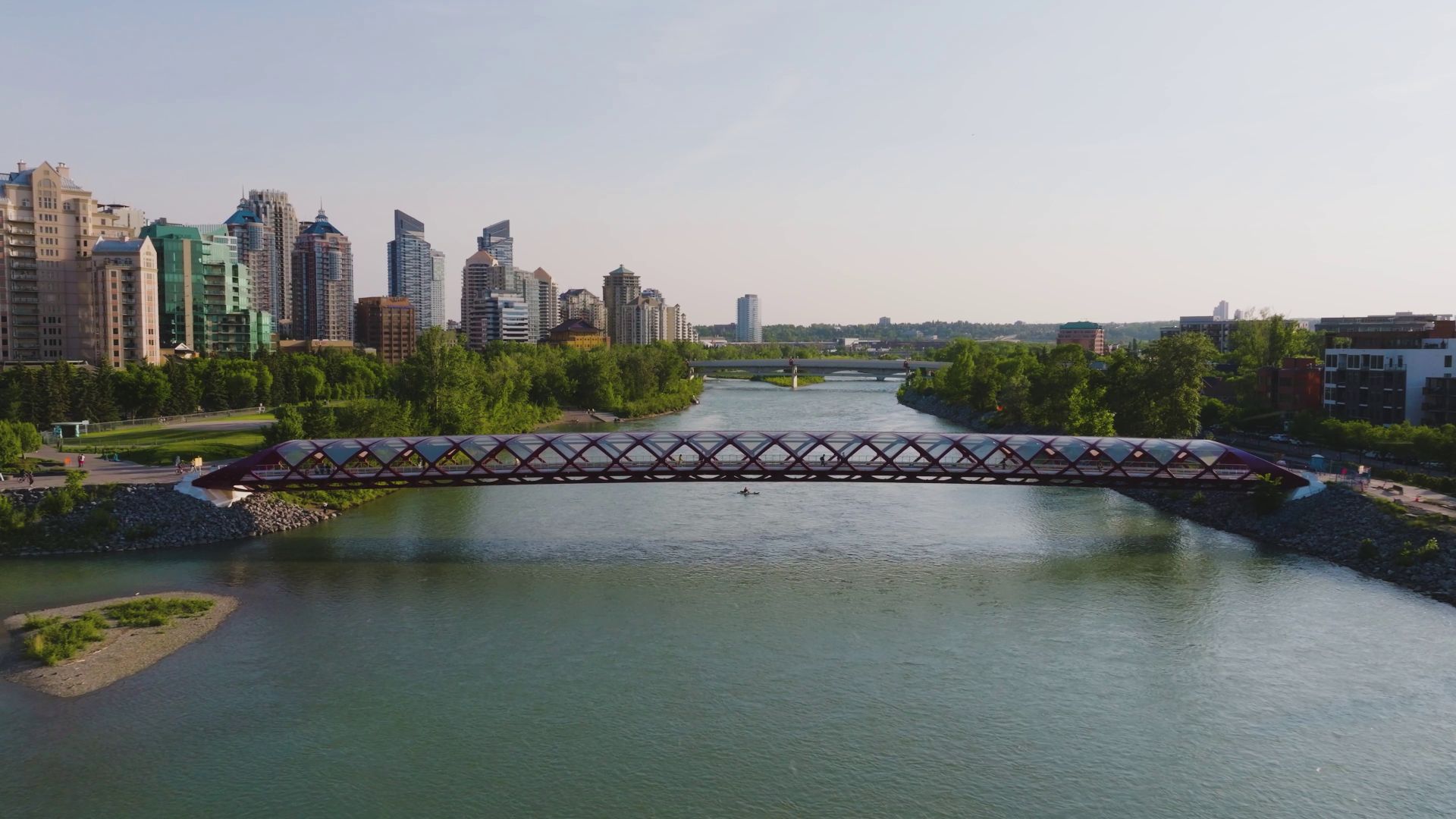 Pedestrians and cyclists crossing the iconic, red-and-white spiraled Peace Bridge on a bright day in Calgary