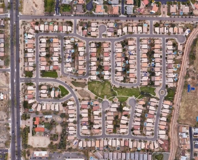 Aerial view of a residential neighborhood with rows of houses, streets, and a central green park area.