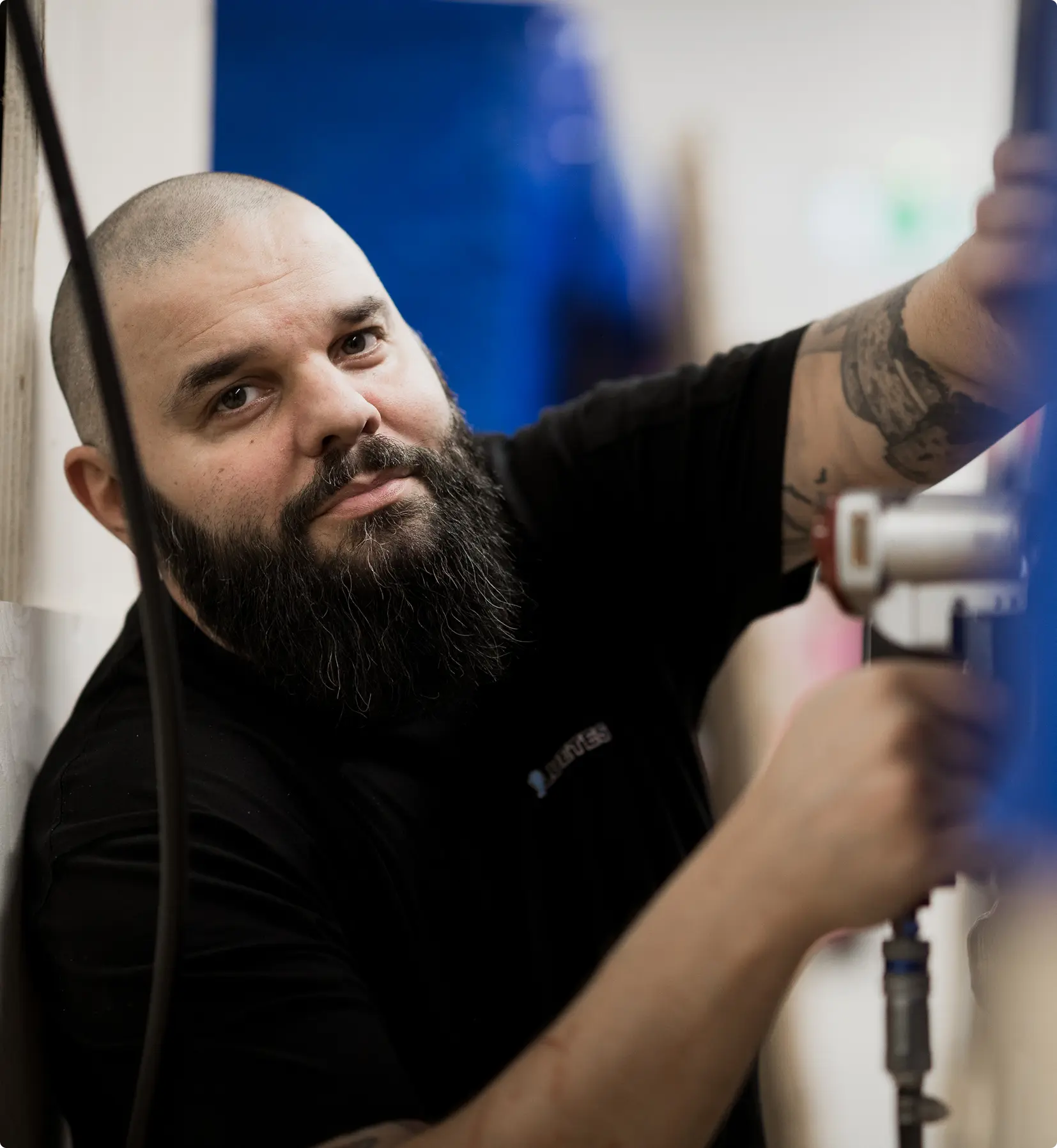 Bearded man with a shaved head wearing a black shirt, working with pipes or machinery.
