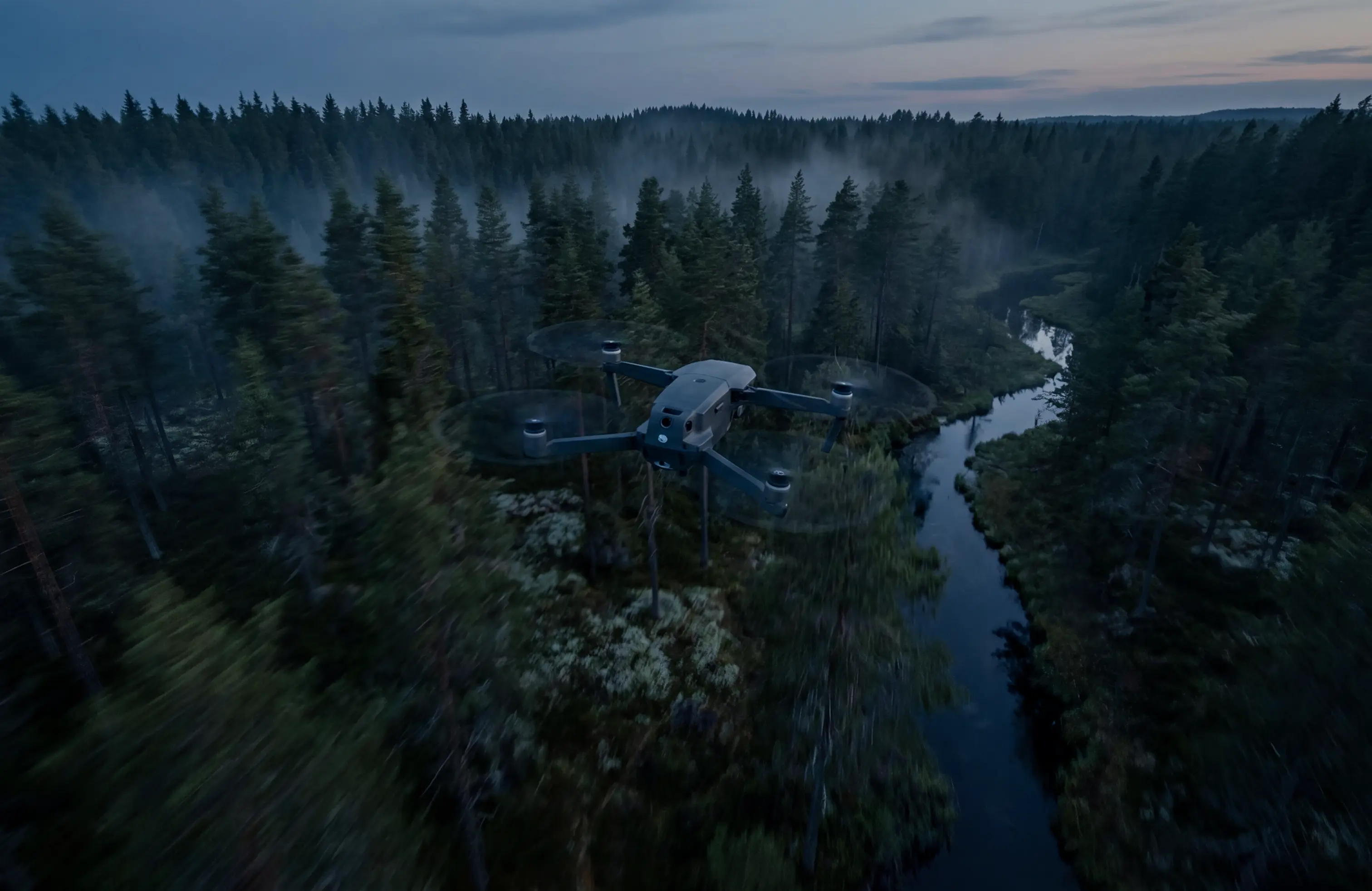 Drone flying over a dense forest with a winding river under a dusk sky.