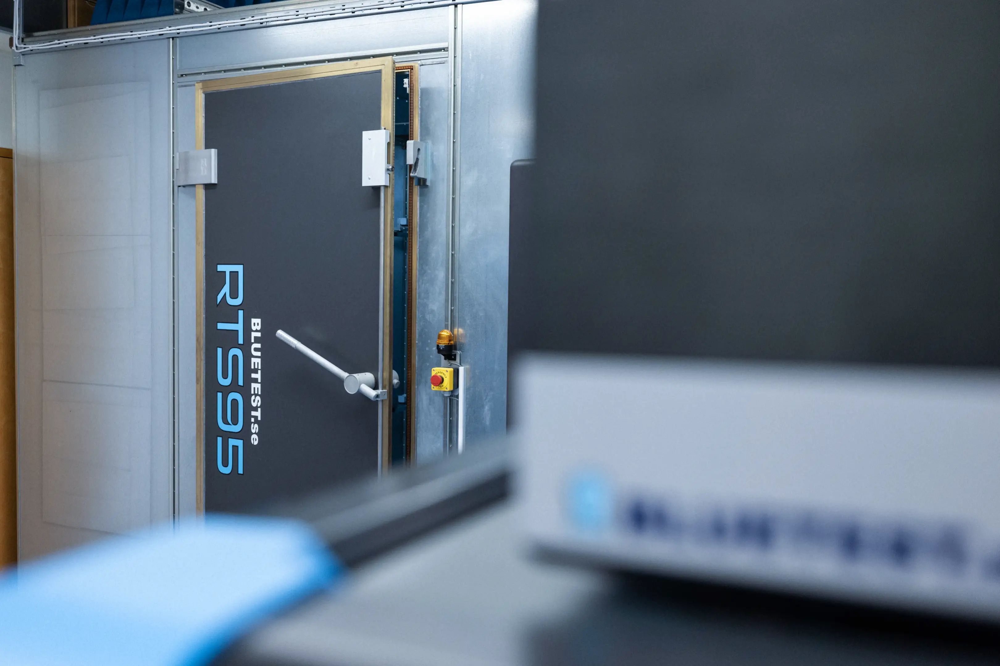 Industrial grey door labeled 'BLUETEST.se RTS95' with a handle inside a metal-framed enclosure.