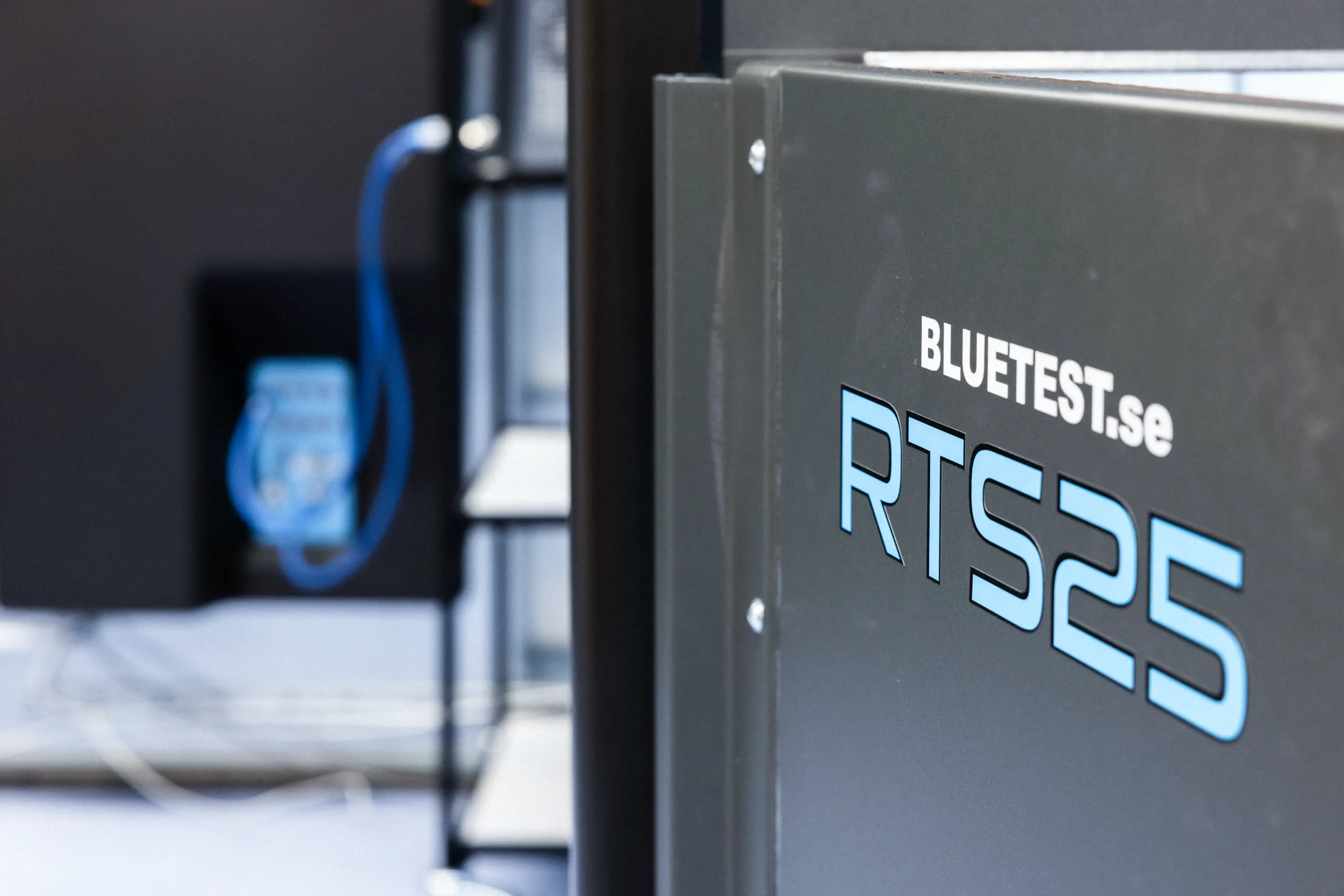 Close-up of a gray device labeled 'BLUTEST.se RT S25' with a blurred background showing a blue connected cable.