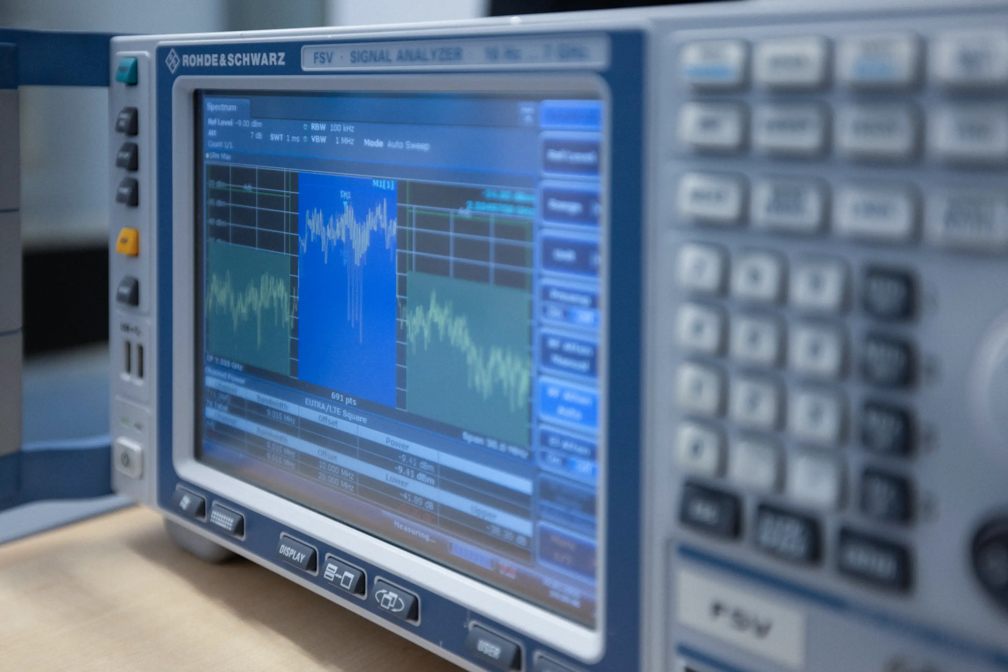 Close-up of a Rohde & Schwarz FSV signal analyzer displaying frequency spectrum data on its screen.