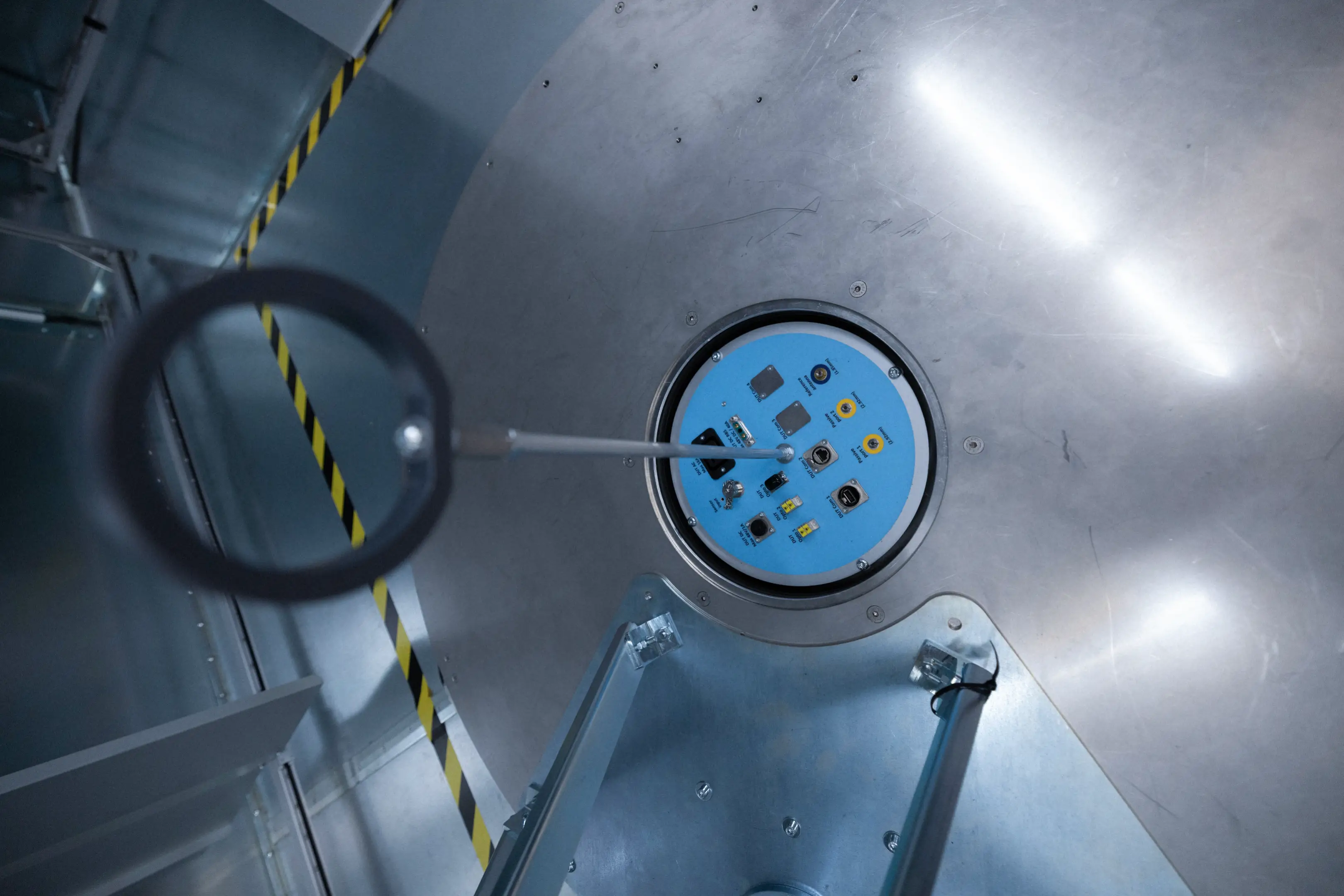 Close-up of a circular metallic panel with a blue control interface featuring various buttons and connectors inside an industrial or laboratory setting.
