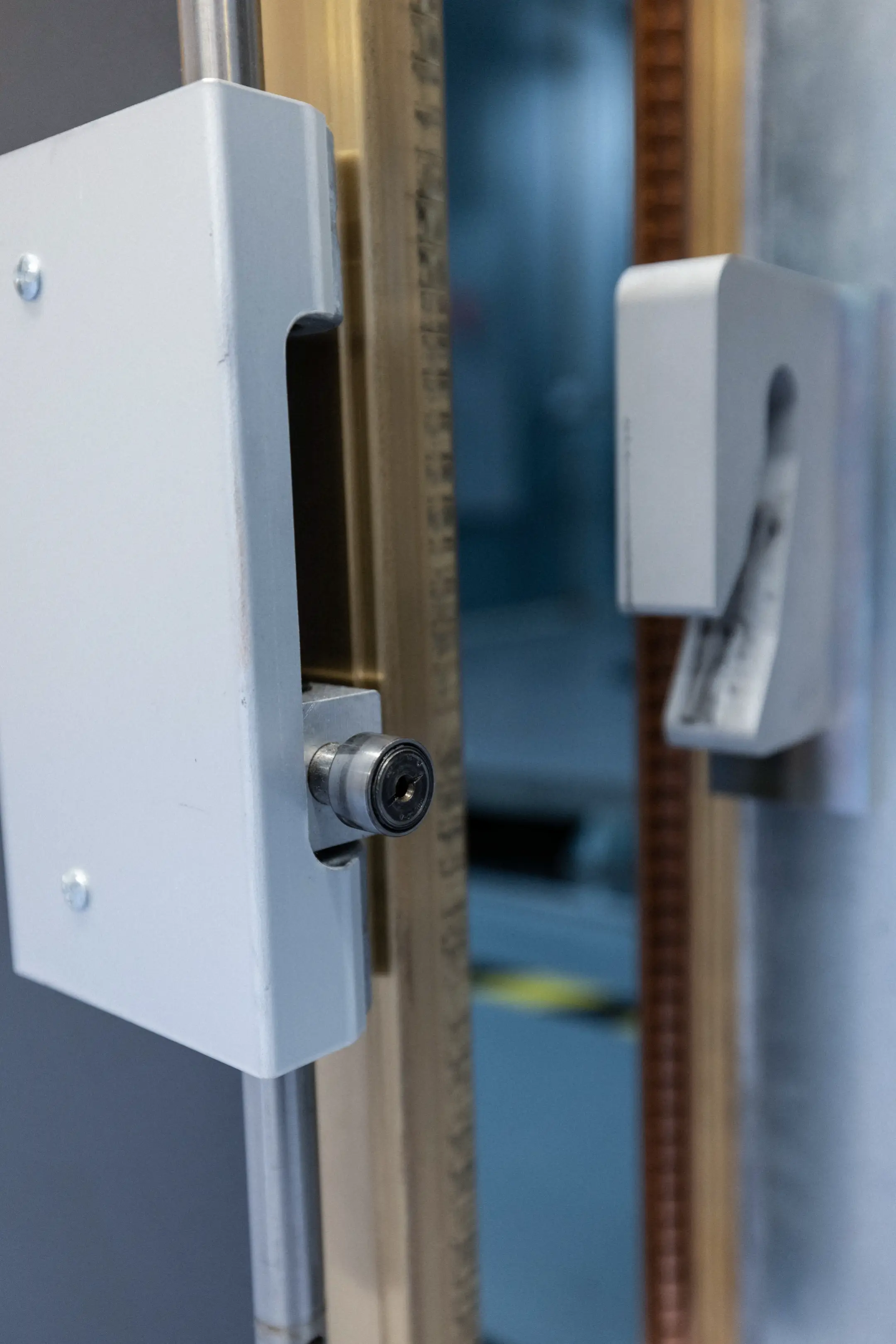 Close-up of a white metal lock mechanism with cylindrical keyhole on a door frame.
