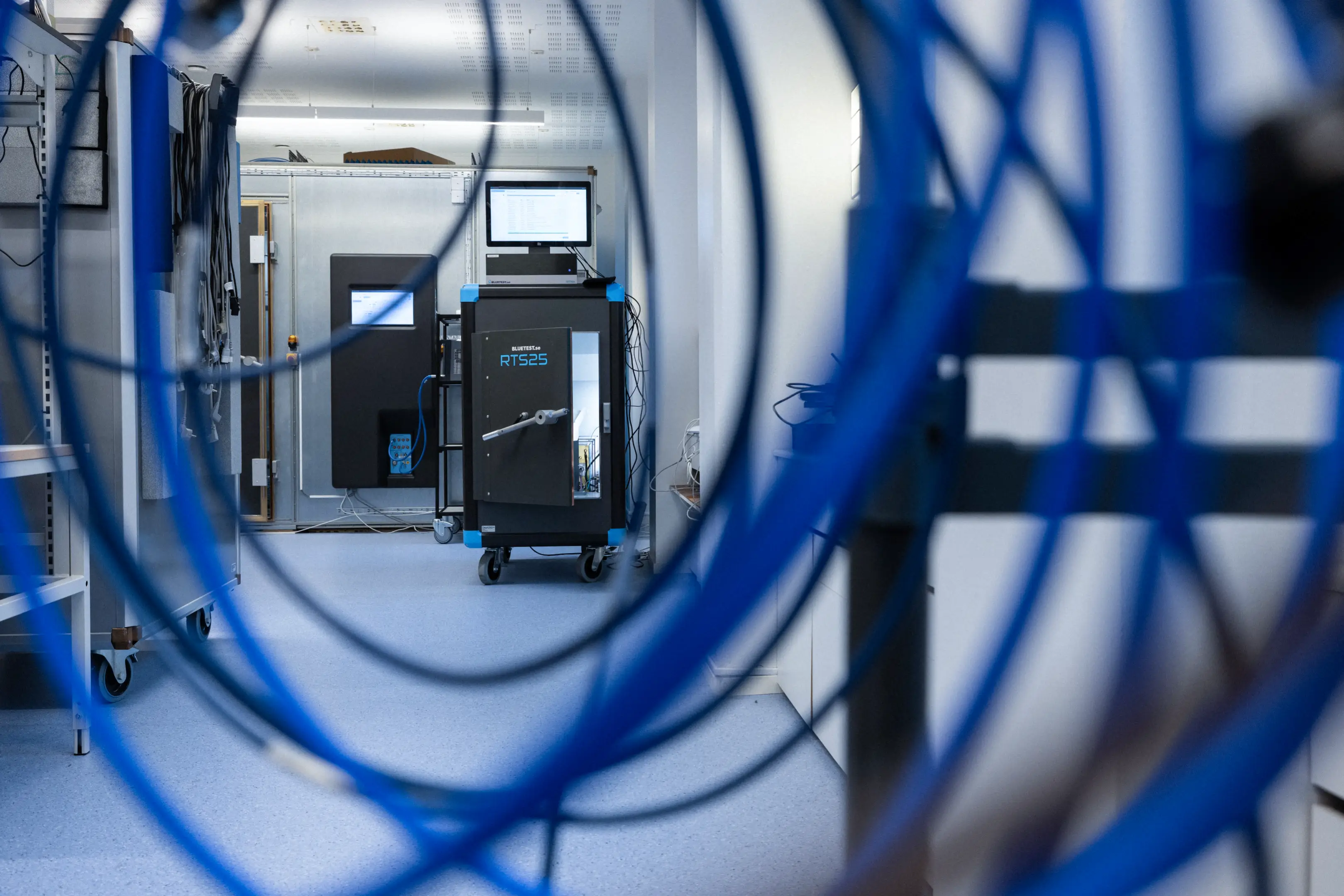 Laboratory room with BLUETEST RTS25 testing equipment seen through coiled blue cables.