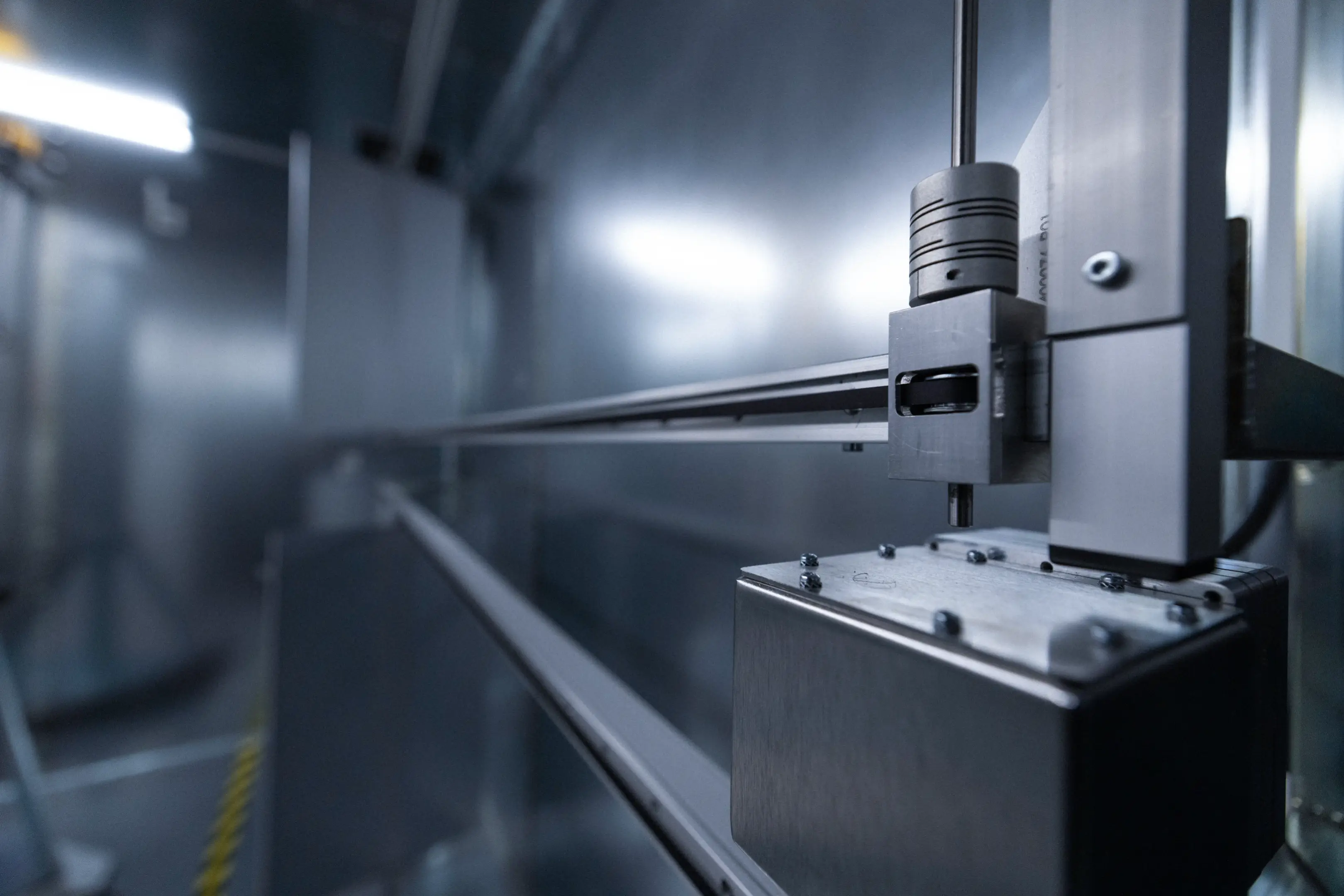 Close-up of a metallic industrial machine or robotic arm inside a factory setting with blue lighting.
