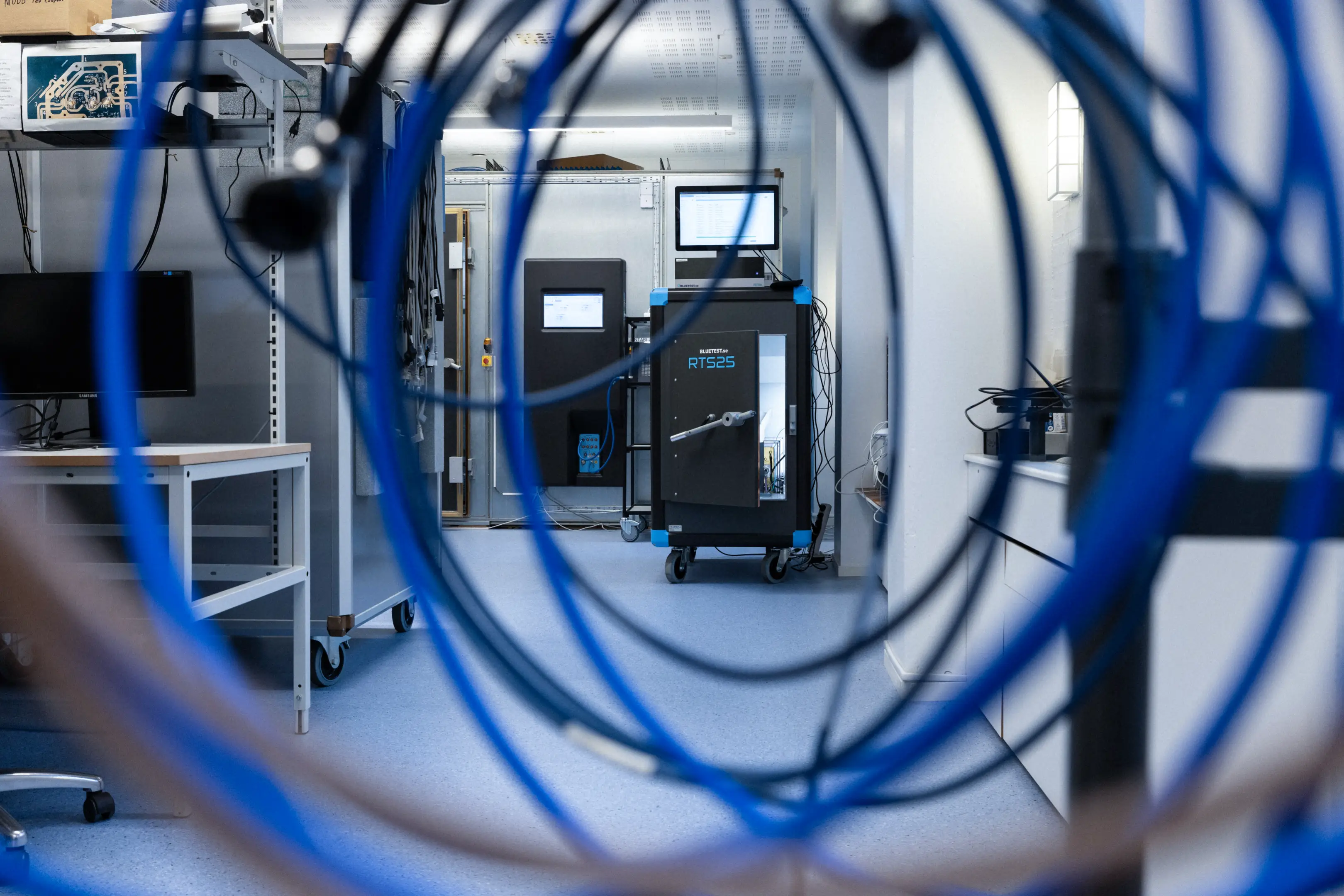 Laboratory room with a Bluetest RTS25 device and a computer seen through coiled blue cables in the foreground.